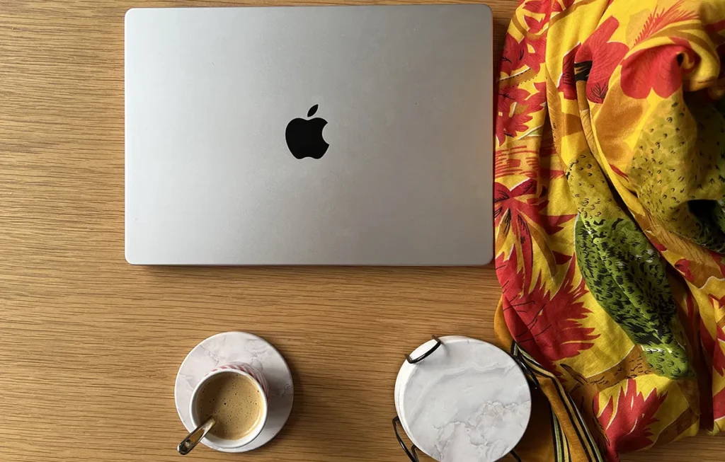 Photo d'un macbook sur une table en bois à côté d'une tasse de café